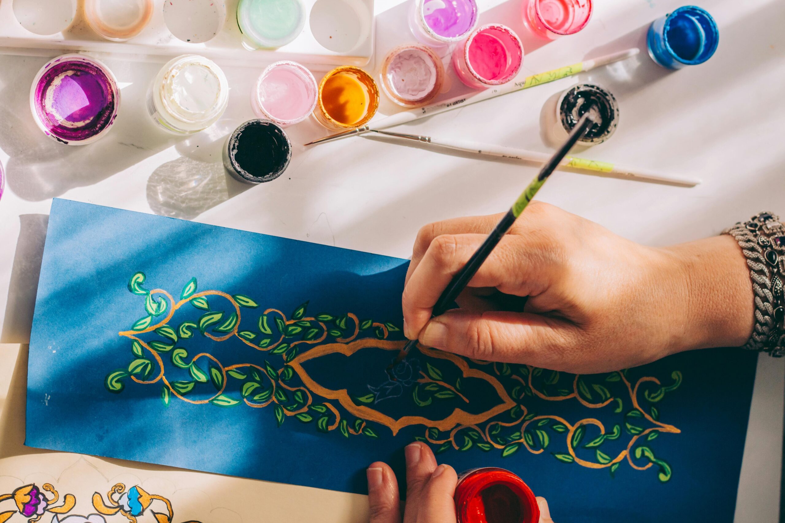 Artistic hand painting intricate design on paper using vibrant colors and brushes.